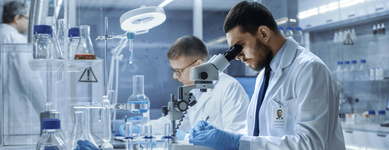 In a Modern Laboratory Two Scientists Conduct Experiments. Chief Research Scientist Adjusts Specimen in a Petri Dish and Looks on it Into Microscope.