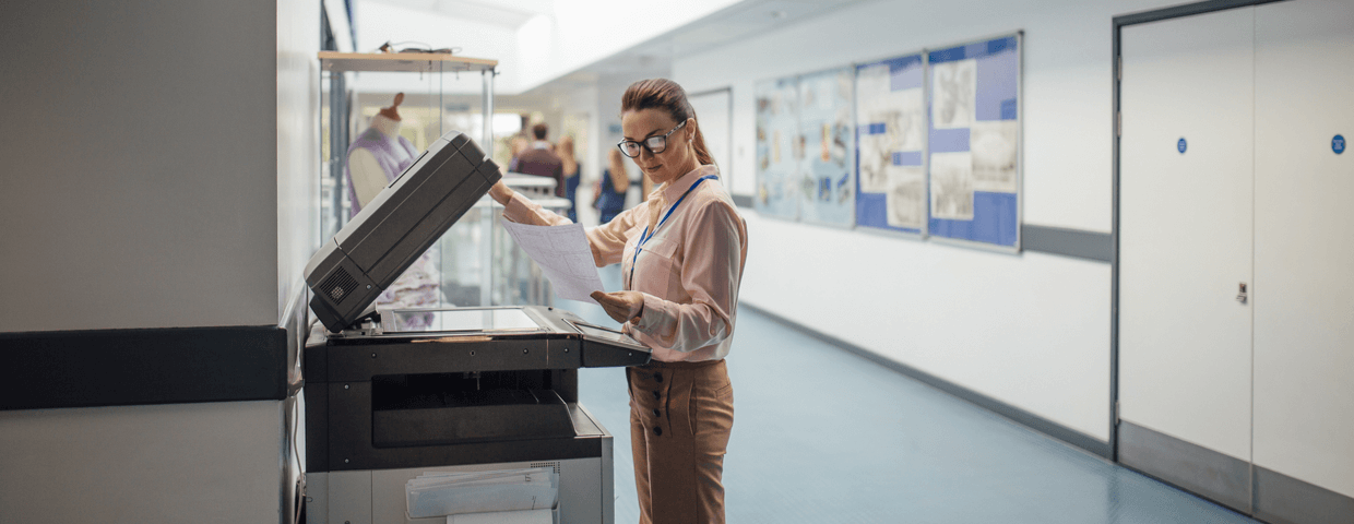 Woman teacher using printer machine in school hallway.