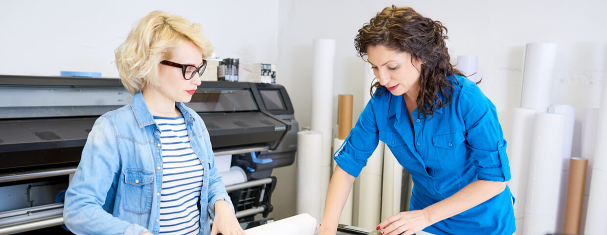 Two woman working next to wide format printer.