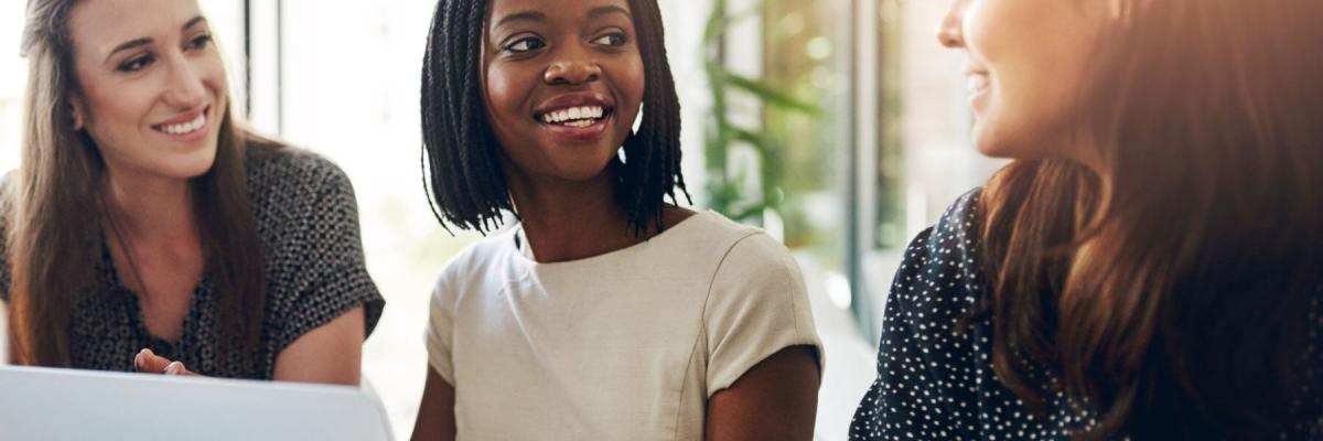 3 employees smiling while talking in front of laptop